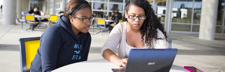 two students sitting at a table working together on a laptop
